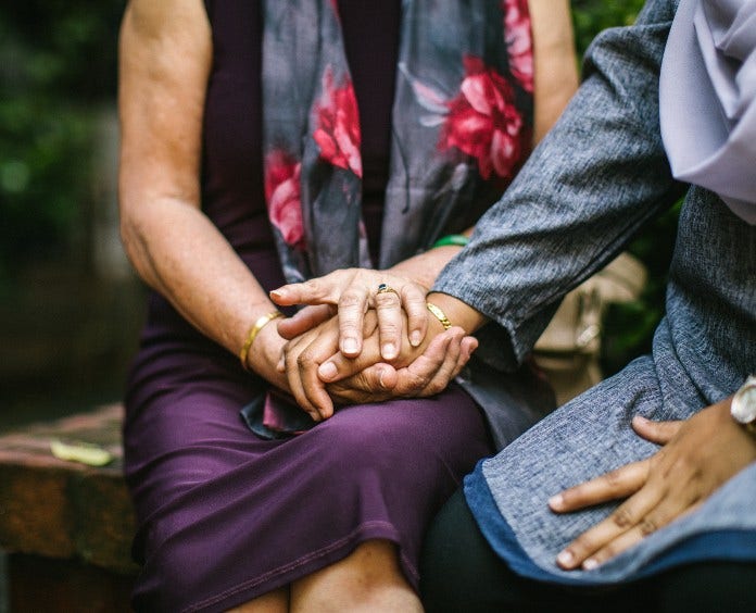 two women sit on outdoor bench as one comforts the other