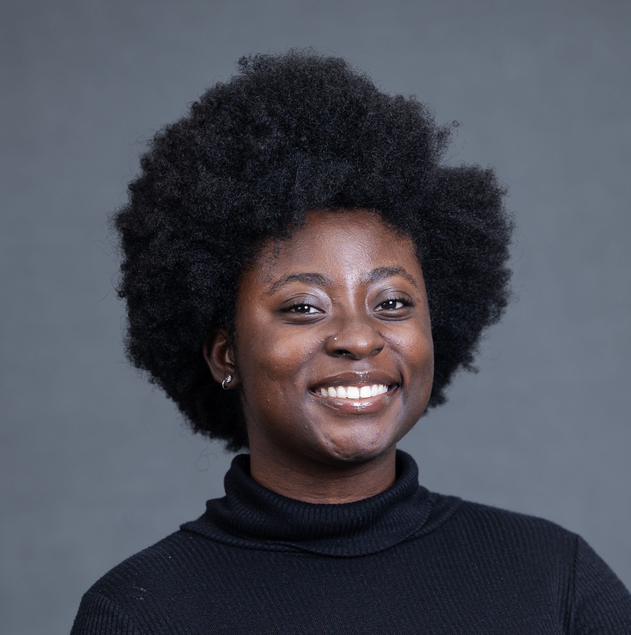 Black woman, smiling, black sweater, afro, stud nose piercing, stud earrings